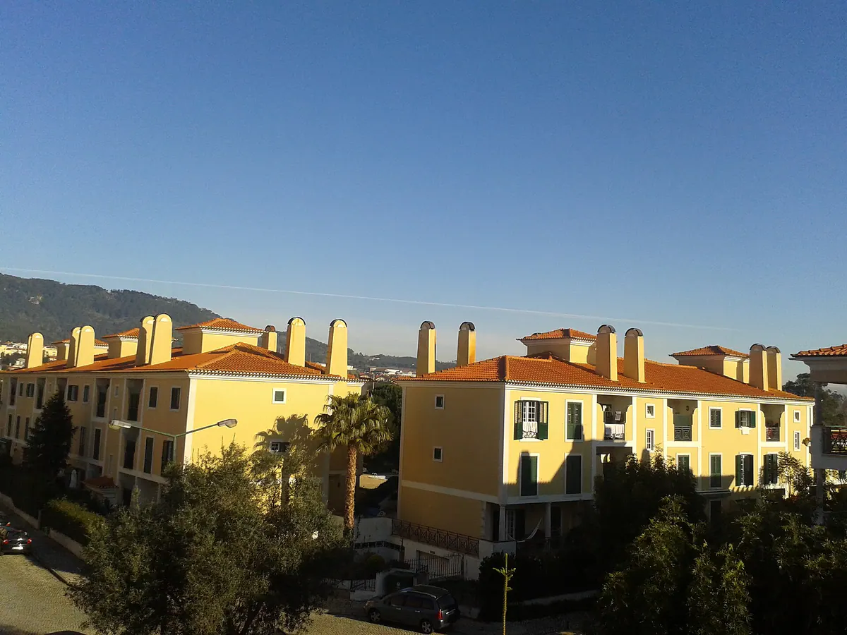 Yellow condominiums with terracotta roofs and palm trees in Beloura, the Sintra hills behind